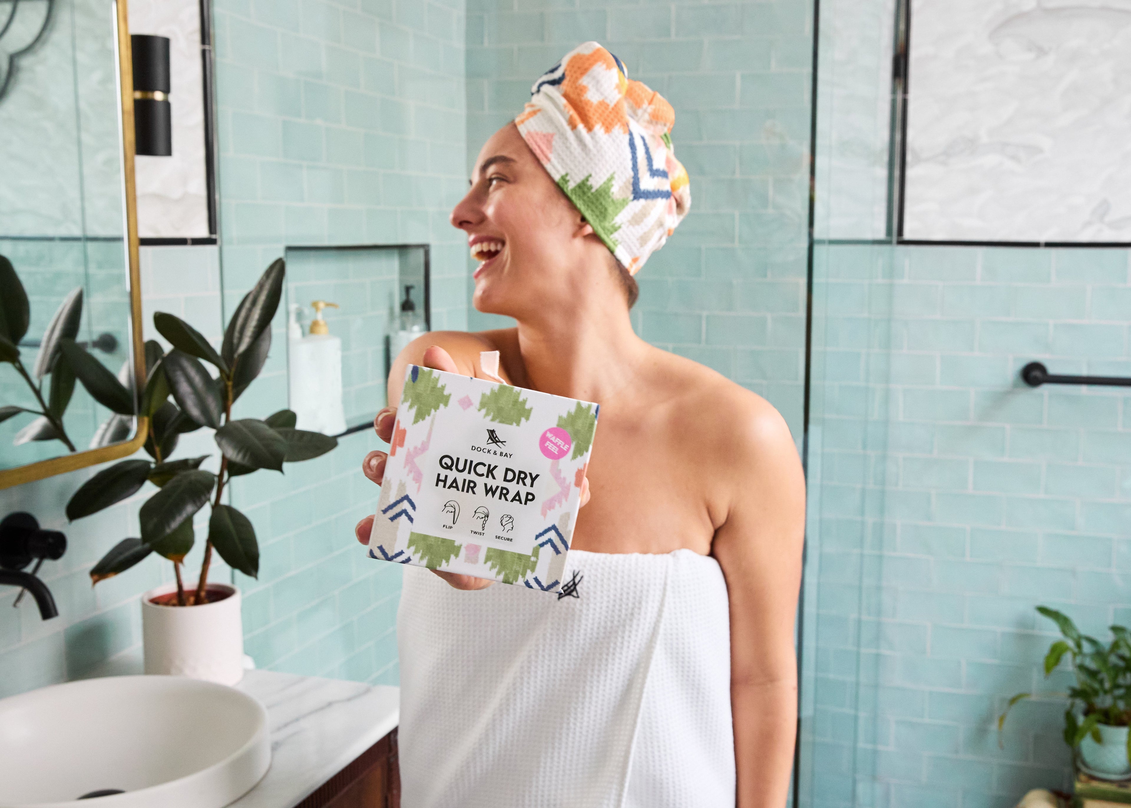 Person in a bathroom holding a quick-dry hair wrap with a plant and mirror in the background