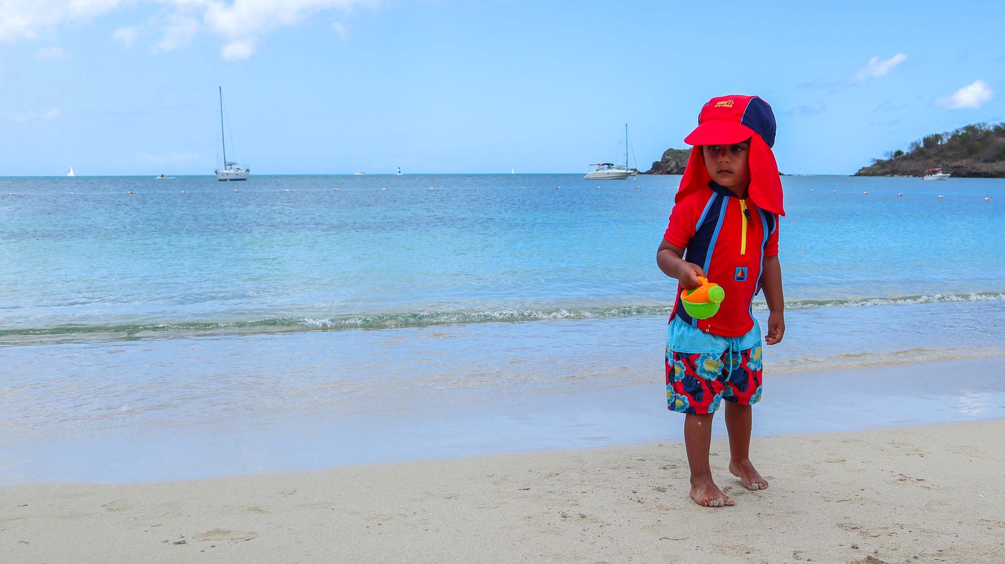 Child on a beach with a colorful towel and hat, ocean and sky in the background