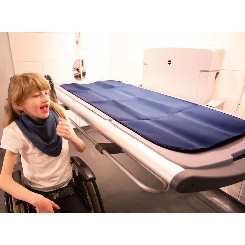 Person in a wheelchair next to a fold down changing  table with the  blue changing mat 