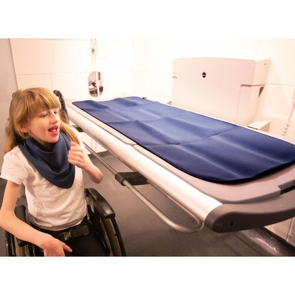Person in a wheelchair next to a fold down changing  table with the  blue changing mat 
