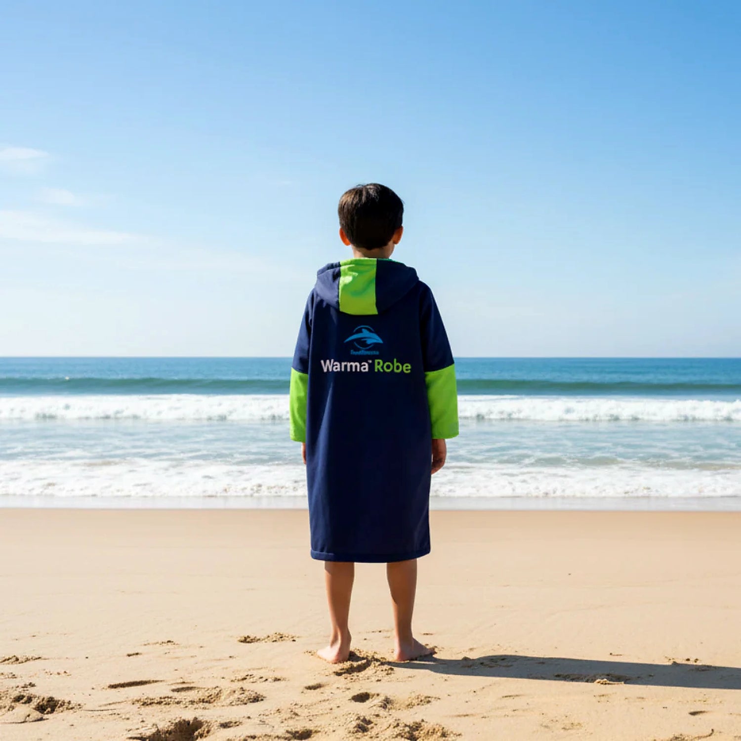Back view of a child wearing the Konfidence kids fleece lined changing robe in navy and lime on the beach